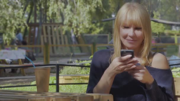 Pretty woman uses phone sitting on the bench in park — Stock Video