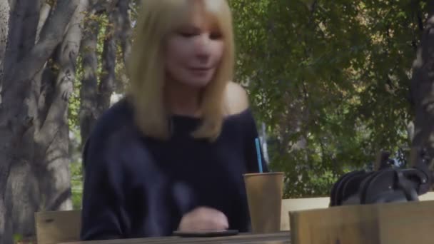 Ładna kobieta używa telefonu i pije kawy siedząc na ławce w parku — Wideo stockowe