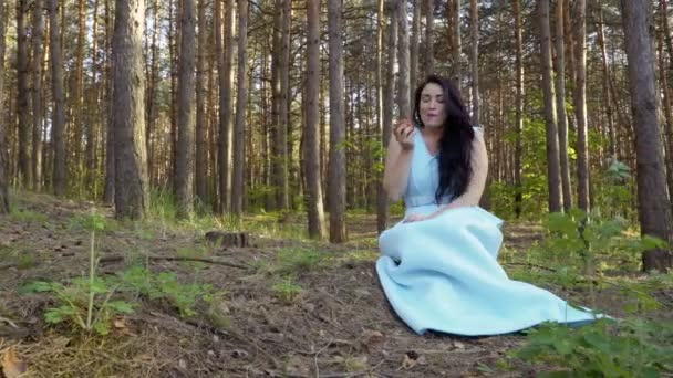 Mooie vrouw in lange blauwe jurk eet appel in het bos — Stockvideo