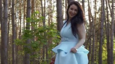 El ormanın içinde mavi elbiseli kamera için poz ayakkabı ile güzel kız