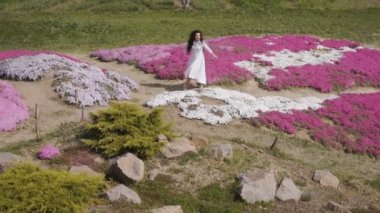 Beyaz elbiseli güzel esmer Pembe çiçek arasında yürüyor