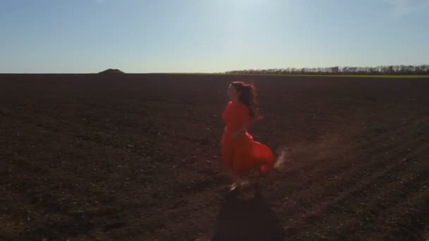 Szczęśliwy beztroski dziewczyna w czerwonej sukience uruchomiona przez zaorane pole — Wideo stockowe