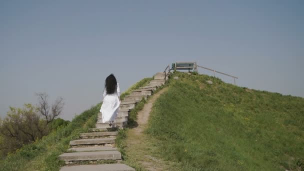 Žena elegance v bílé dlouhé šaty pohyblivých schodech na zeleném kopci — Stock video