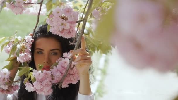 Krásná žena vypadá ve fotoaparátu prostřednictvím květy růžové sakura — Stock video