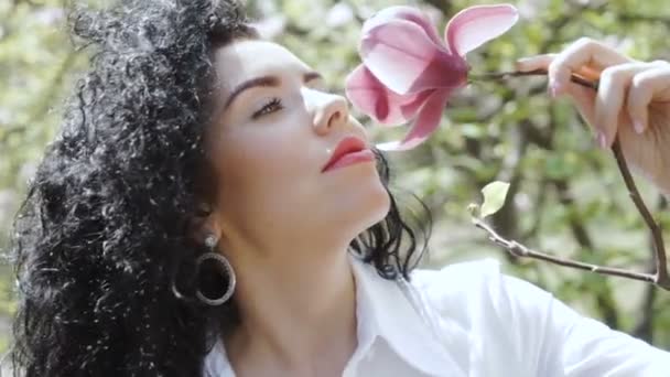 Чарівна кучерява брюнетка насолоджується запахом квітки магнолії — стокове відео