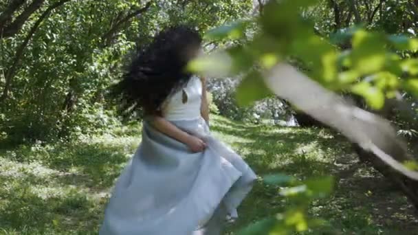Брюнетка в синем платье прогуливается по саду в слоупстайле — стоковое видео