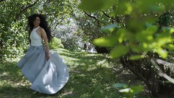 Encantadora morena mueve su vestido largo de pie en un jardín verde — Vídeos de Stock