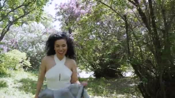 Mooi lachen brunette draait op de camera via een zomertuin — Stockvideo
