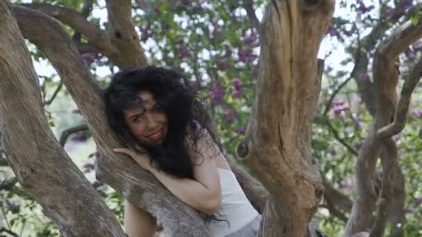 Lindo sorriso morena lixívia no tronco da árvore — Vídeo de Stock