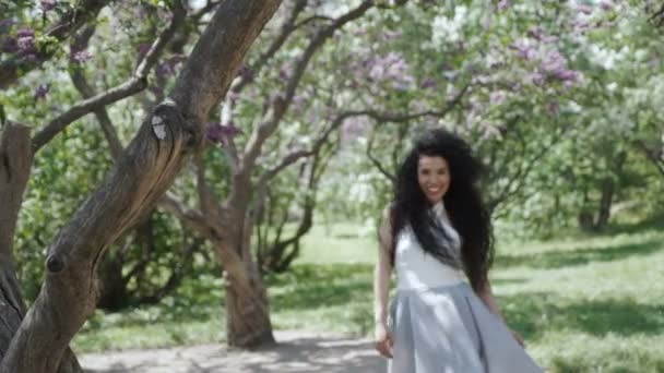 Hermosa mujer en vestido largo sonriendo a la cámara de pie en el jardín de verano — Vídeos de Stock