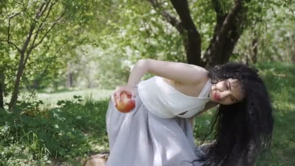 Красивая брюнетка ест красное яблоко в саду — стоковое видео