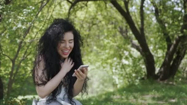 Szczęśliwa kobieta wiadomości z przyjaciółmi za pomocą jej telefon i zrelaksować się w ogrodzie — Wideo stockowe