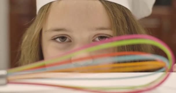 Extreem close-up portret van een schattig blank meisje met diep bruine ogen. Klein brunette kind met koksmutje kijkend naar veelkleurige garde op de voorgrond. Bioscoop 4k beelden Prores Hq. — Stockvideo