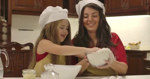 Küçük beyaz kız tabaktan un dökmesi için annesine yardım ediyor. Çocuk burnuna dokunuyor ve yüzünde beyaz bir leke bırakıyor. Mutlu gülümseyen aile yemekleri. Sinema 4k görüntüleri Prores Hq. — Stok video