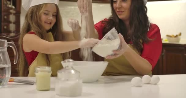 Кавказская мать и дочь выливают муку из тарелки. Маленькая девочка помогает маме готовить. Счастливой счастливой семейной выпечки. Съемки в кинотеатре 4k . — стоковое видео