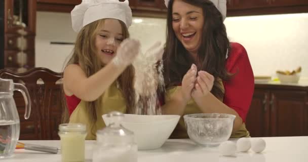 キッチンで一緒に調理する陽気な白人の母親と娘。小さな女の子の手と小麦粉の周りを飛んで拍手。家で焼きながら笑っている幸せな家族。映画4k映像｜Prores Hq. — ストック動画
