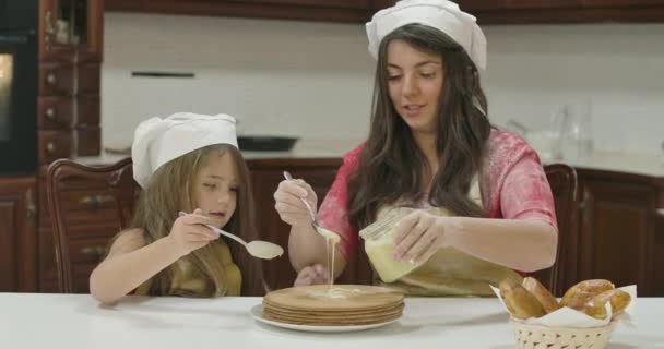 Mère et fille caucasiennes appliquant du lait condensé sur un gâteau cuit au four. Joyeux famille dans les chapeaux de cuisine et tabliers de cuisine ensemble à la cuisine à la maison. Cinéma 4k séquences ProRes HQ . — Video