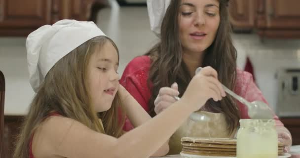 Маленька кавказька дівчинка, яка разом зі своєю веселим матусею споживає солодке конденсоване молоко. Щаслива мама і дочка готують їжу і розважаються вдома. Відеозапис фільму 4k Prores Hq. — стокове відео