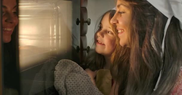 Close-up gezichten van het kleine blanke brunette meisje en haar moeder die in de oven kijken. Gelukkig glimlachend familie bakken in de keuken thuis. Bioscoop 4k beelden Prores Hq. — Stockvideo