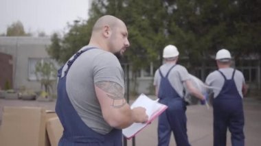 Yetişkin sakallı beyaz bir adamın portresi yol faturasına paketleri alıp giden iki işçi olarak yazıyor. Taşıma servisinde çalışıyorum..