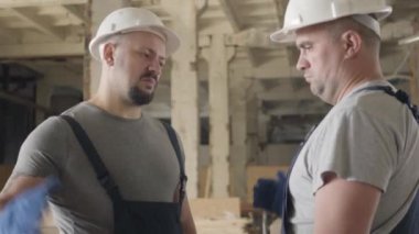 İnşaat alanında beyaz kasklı iki güçlü Kafkasyalı inşaatçı el sıkışıyor. İşçiler evet diyor ve bir adam gidiyor..