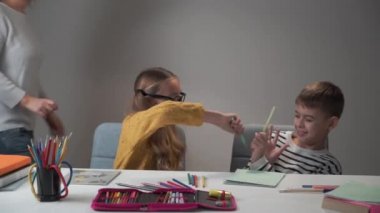 Gözlüklü beyaz kız ve erkek sınıf arkadaşı renkli kalemlerle kavga ediyorlar. Yetişkin bir kadın geliyor ve onları sakinleştiriyor. Okulda oynayan neşeli çocuklar..