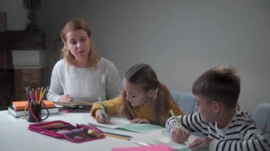 Evde iki öğrenciye öğretmenlik yapıyor. Beyaz çocuk ve kız ödev yapıyor. Egzersiz kitaplarında yazan çocuklar ve görev veren genç bir kadın. Eğitim, istihbarat, ilkokul.