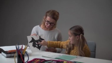 Kafkasyalı kız Rorschach 'ın test kartını gösterip vizyonunu açıklıyor. Çocuğa teşhis koyan beyaz kadın psikolog. Okuldaki psikolog muayenehanesinde sınavı geçen öğrenci..