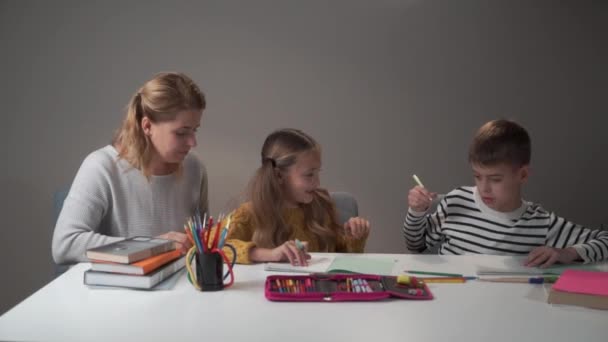 Retrato de dos niños caucásicos y una maestra joven sentada a la mesa y hablando. Tutor enseñando a los niños en la escuela primaria. Educación, inteligencia, aprendizaje . — Vídeos de Stock