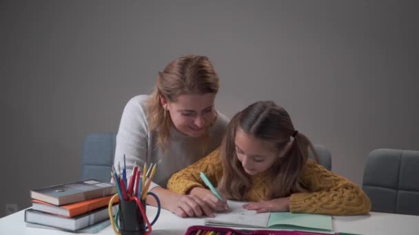 Retrato de una joven tutora caucásica ayudando a su estudiante a hacer los deberes. Linda chica caucásica escribiendo en el libro de ejercicios. Profesor de educación escolar. Concepto de educación, escuela primaria . — Vídeos de Stock