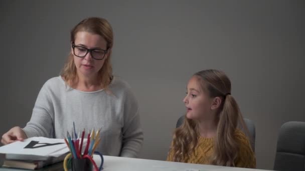 Retrato de um tutor caucasiano feminino em óculos e uma menina aprendendo alfabeto. Professor jovem inteligente mostrando cartão com a letra A e explicando a pronúncia correta . — Vídeo de Stock