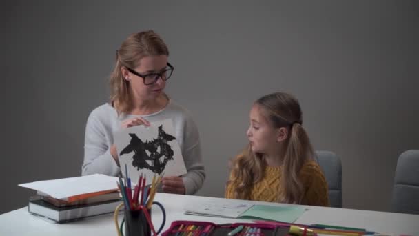 Vrouwelijke Kaukasische psycholoog toont Rorschach test kaart aan het kleine meisje. Schattig kind slaagt voor test in het psychologen kantoor op school. — Stockvideo