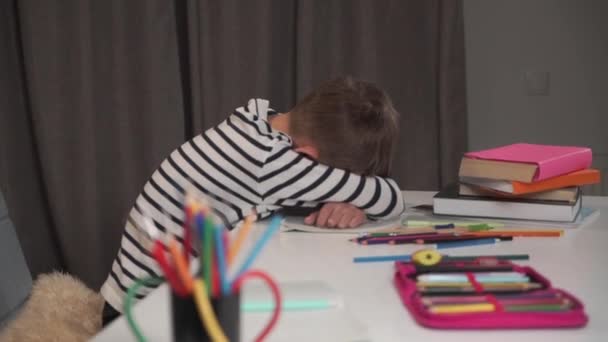 Pequeño colegial caucásico durmiendo en su libro de ejercicios en la mesa. Niño cansado después de hacer la tarea en casa. Niño con chaqueta a rayas agotado después de estudiar. Cámara moviéndose de izquierda a derecha . — Vídeos de Stock