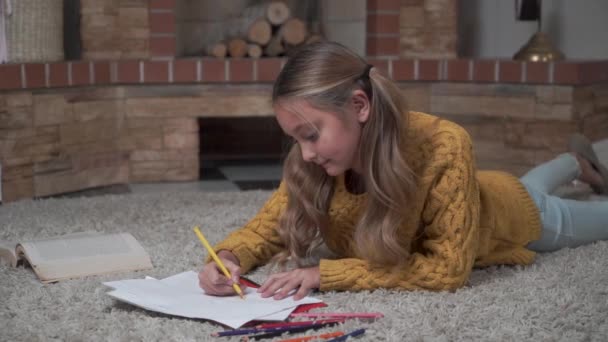 Ritratto di una graziosa ragazza caucasica con lunghe code di cavallo posate sul morbido tappeto e sul disegno. Un bel bambino che riposa nei fine settimana a casa. Quadro creativo artista pittura. Infanzia, tempo libero . — Video Stock