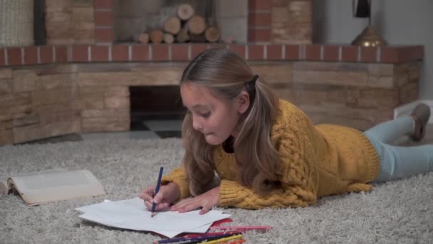 귀여운 코카서스 여자 애가 부드러운 카펫에 누워 그림을 색칠하는 것을 클로즈업합니다. 예쁜 아가씨가 주말에 집에서 쉬고 있어. 그림그리는 예술가. 아동기, 여가 시간. — 비디오