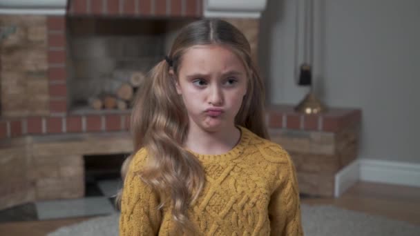 Retrato de una niña caucásica molesta en suéter de mostaza sentada frente a la chimenea en casa. Niño triste cruzando las manos en el pecho . — Vídeo de stock