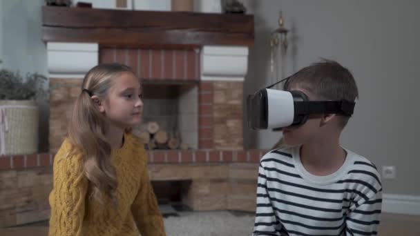 Schattige blanke zus wachtend op haar broer om te spelen in Vr bril. Broers en zussen zitten thuis voor de open haard. Weekenden, vrijetijdsbesteding, rusten, kindertijd. — Stockvideo