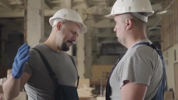 Bâtisseur barbu caucasien avec tatouage sur l'épaule tremblant collègues main et souriant. Deux hommes travaillant sur le chantier . — Video