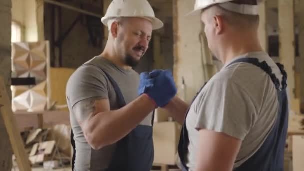 zwei kaukasische Bauarbeiter, die sich die Hände schütteln und lächeln. zwei Männer, die auf der Baustelle arbeiten. Mitarbeiter in weißen Schutzhelmen zufrieden mit ihrer Arbeit.