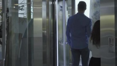 Kendine güvenen beyaz bir adam ve küçük tatlı bir kız modern cam asansöre giriyor. Baba düğmeye basıyor ve asansör yukarı çıkıyor. Aile, gidiş ya da varış bölgesinde. Turizm, seyahat, seyahat.