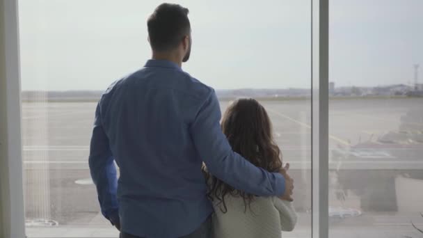 Vista posterior de hombre caucásico barbudo guapo en ropa casual de pie con su encantadora hija en el fondo de la ventana del aeropuerto. Niña bonita esperando la salida o llegada con el padre . — Vídeos de Stock