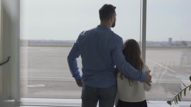 На згадку про дорослого кавказького чоловіка, який стояв з маленькою дівчинкою в аеропорту і дивився на вікно. Дочка чекає на від'їзд або прибуття з батьком. Подорожі, туризм, вихідні. — стокове відео