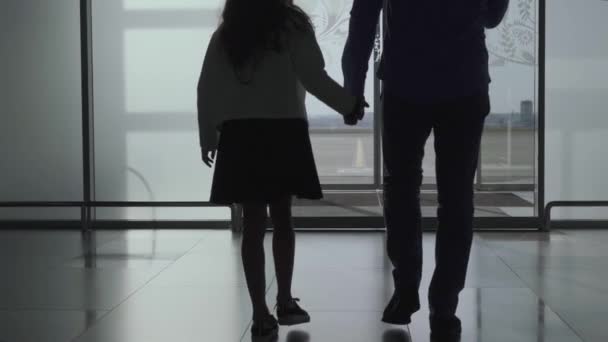 Vue de dos silhouettes de l'homme et de la fille caucasiens qui sortent de la porte en verre. Un jeune père et sa fille vont sur la piste de l'aéroport. Voyager ensemble, tourisme . — Video