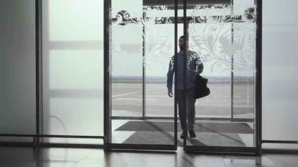 Молодой бородатый кавказский мужчина входит в стеклянную дверь аэропорта с багажом. Маленькая веселая девочка подбегает к отцу. Парень обнимает и крутит свою дочь Прибытие, встреча за поездкой, туризм . — стоковое видео