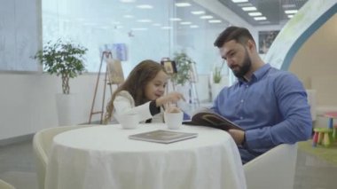 Zengin beyaz adam ve küçük kız havaalanında Vip bekleme salonunda oturuyor, resimlere bakıyor ve çay ya da kahve içiyor. Baba ve kızı ayrılmadan önce birinci sınıftan dinleniyorlar..