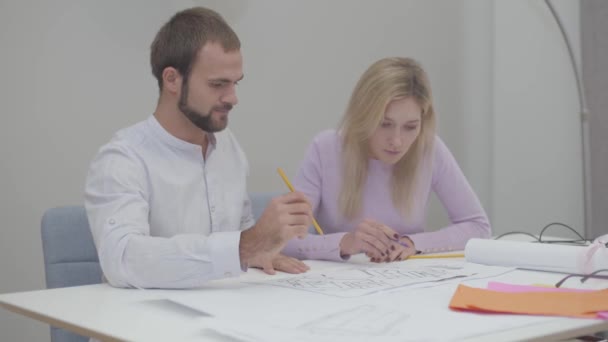 Intelligente vrouwelijke blanke ontwerper tekent blauwdrukken op kantoor. Professioneel lesgeven aan mannelijke assistent om tekeningen te maken. Specialisten die ideeën op papier uitvoeren. — Stockvideo