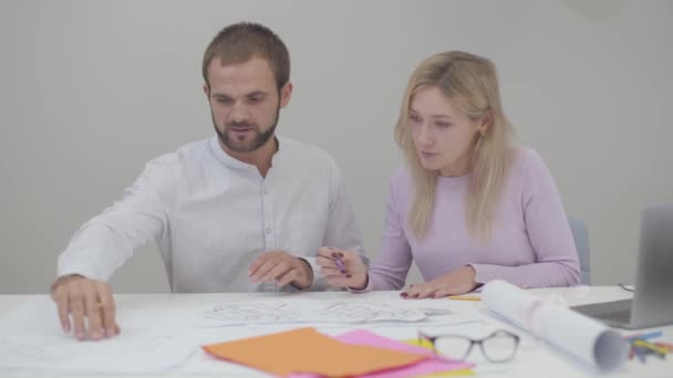 Dois designers profissionais caucasianos a ver plantas no escritório. Jovem mulher bonita e homem bonito implementando ideias no papel . — Vídeo de Stock