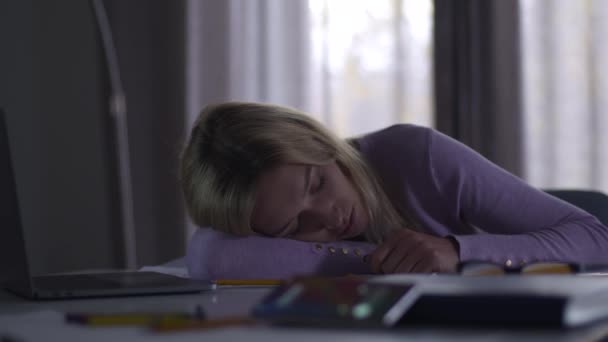 Young blond Caucasian woman sleeping at the table in office. Her mobile phone ringing at the foreground. Young tired professional architect or designer spending evening at work. Overwork, hardworking. — Stock Video