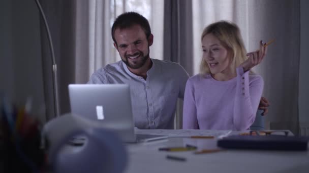 Vrolijke blanke collega 's die in de laptop kijken en lachen. Mannelijke en vrouwelijke professionals kijken grappige video of foto online. Architecten of ontwerpers die 's avonds op de werkplek rusten. — Stockvideo