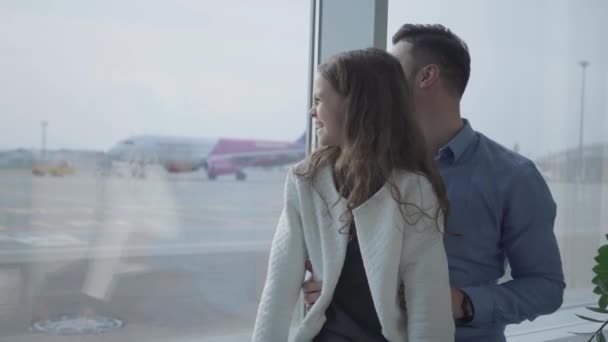 Крупный план симпатичной белой девушки с вьющимися волосами, смотрящей на взлет самолета со своим отцом. Мужчина сидит со своей дочерью на подоконнике аэропорта и смотрит на взлетно-посадочную полосу. Путешествия, туризм . — стоковое видео